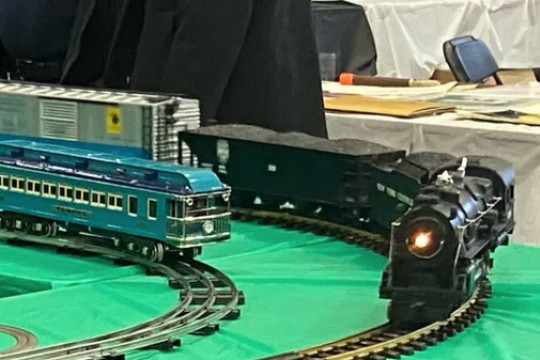a model train comes around a corner on a green table cloth set with tracks. Another train sits next to it.