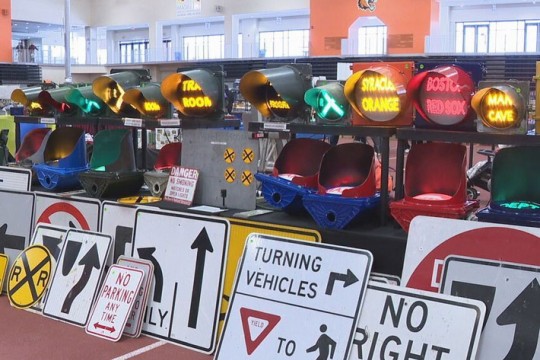 lighted train crossing signs sit behind metal train type caution signs at an event.