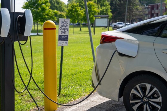 A photo showing an outdoor electric vehicle charging station. A silver car is plugged into the charging station and parked in a spot that is labeled electric vehicle charging only.