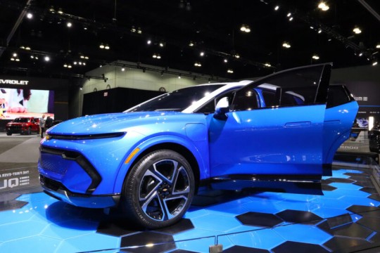 A photo of a blue car in a showroom. The car is some sort of SUV and is placed on a black and blue pedestal to compliment the bright blue paint of the car.