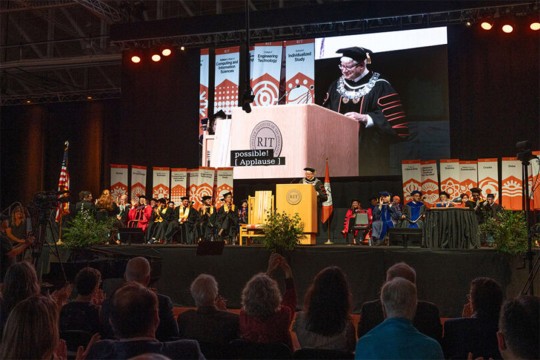 a man stands on a stage addressing a crowd.