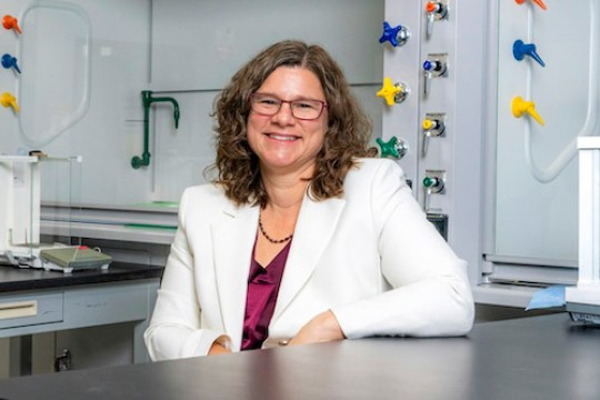 Caroline Solomon sits at a table in a lab in a white blazer.