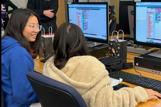 two young girls sit next to each other at a computer.