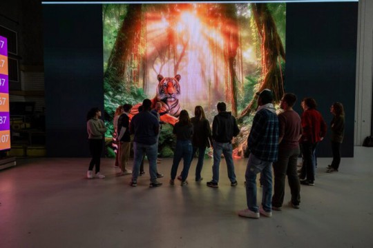 a group of people stand in front of a large generated image of a tiger in the jungle.