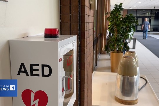 an A E D device is attached to a wall in a busy common area of a college.