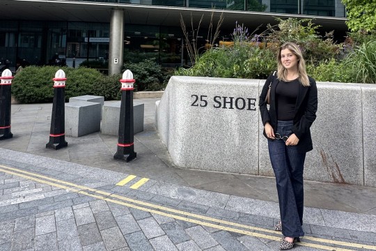 'a woman dressed in a black top and jeans stands in a public plaza.'