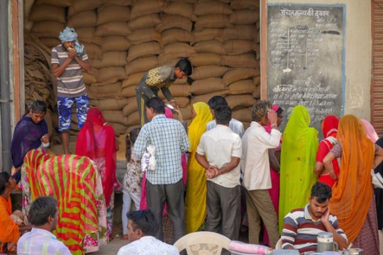 people in colorful clothing stand in a line to get food rations.