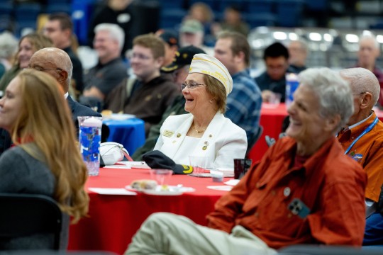 a woman sits at a table watching a speaker