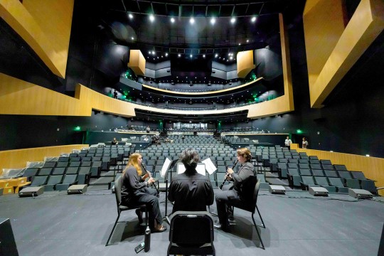 students in an orchestra test acoustic settings on a stage