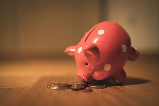 a pink piggy bank sits on a table with some coin change.