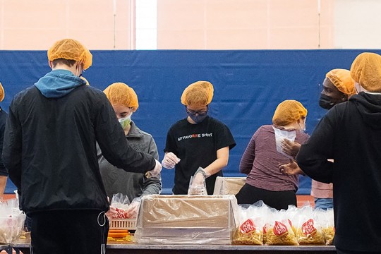 students with orange hair nets pack food for distribution