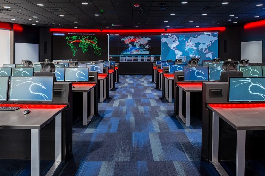 a classroom filled with computers and a backdrop of information displayed on electronic boards at the front of the room.