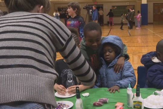 children sit at a table decorated for putting together an art project in a gymnasium.