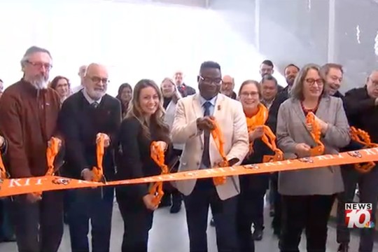 several adults cut an orange R I T ribbon with large scissors.