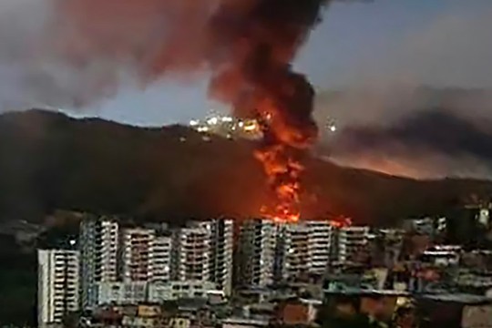 A set of tall buildings on fire with hills in the background