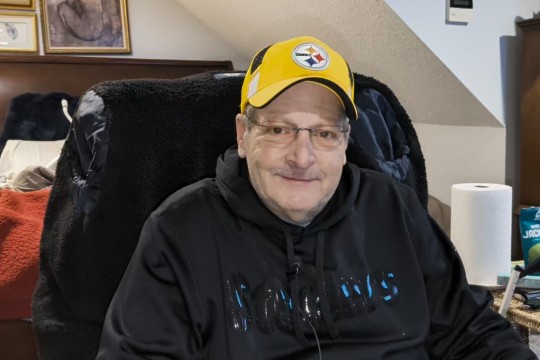 Man sits at home wearing a yellow Steelers hat.