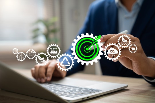 icons of gears appear overlayed on top of an image of a person typing on a laptop