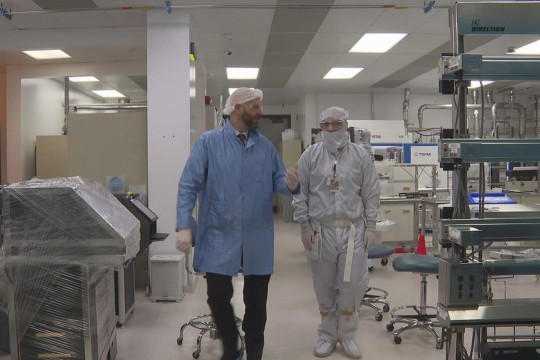 two people in clean room gear wallk through a labratory environment.
