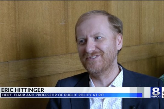 a man speaks to W R O C T V with his name on a banner beneath him