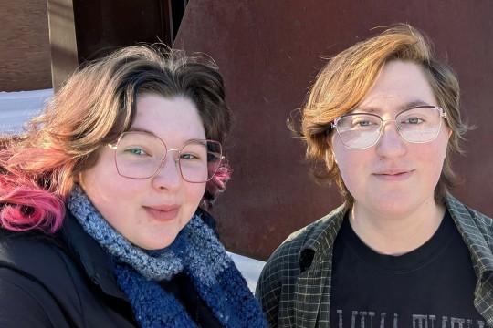 'two people smile for the camera in front of an iron wall.'
