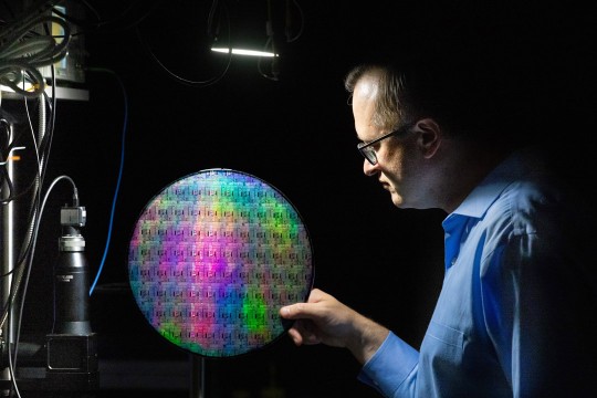 'a man in profile holds a quantum photonic wafer against a black background.'