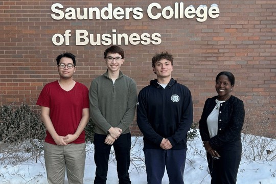 'a group of four people stand in front of a brick building labeled Saunders College of Business'