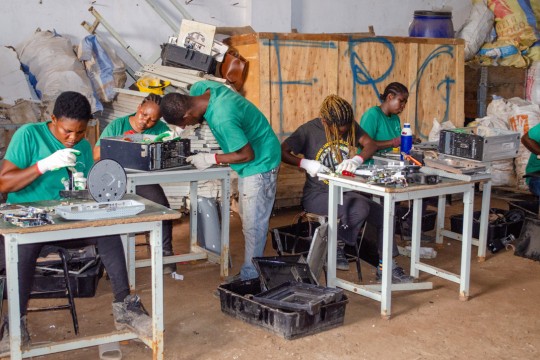 'People work at a small tables at an electronic recycling facility.'