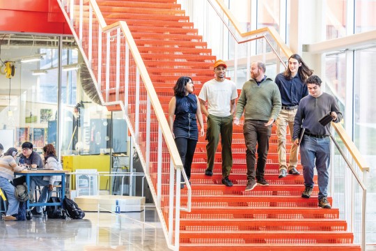 'a group of people walk down orange steps in a brightly lit modern atrium.'