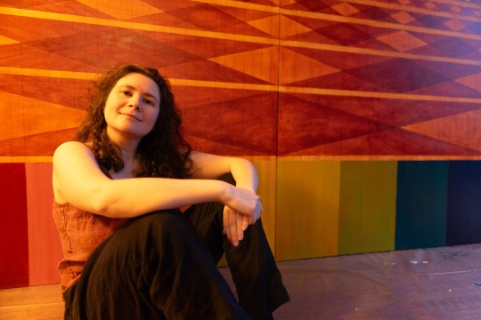 'a woman in a red tank top and black pants sits on the floor in front of a geometric art display.'
