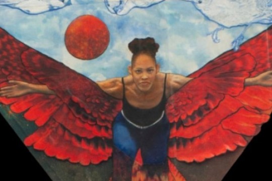 a woman poses with illustrated wings behind her on a wall