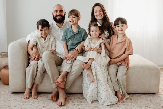 a family of six sits on a neutral colored couch in a brightly lit livingroom