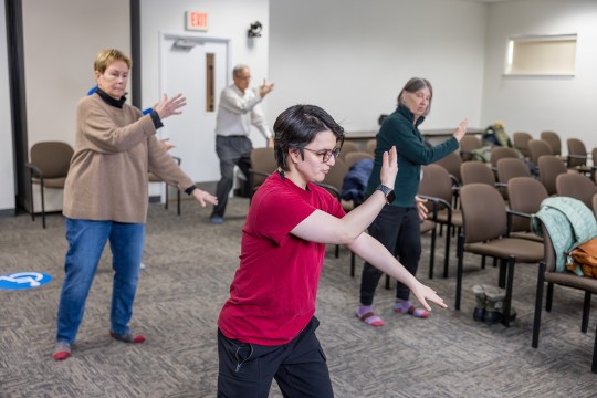'three people practive Tai Chi in a classroom environment.'