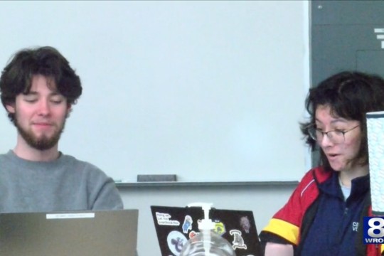two students sit in front of laptops working together.