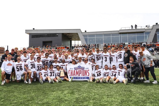 the R I T Mens lacrosse team sits in front of the new Judson stadium holding a champions sign
