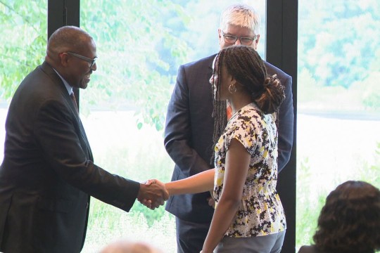 RIT President Bill Sanders looks on as a student shakes hands with a man during a Rochester City Scholars event.