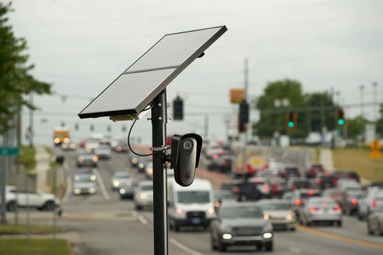 a license plate reader stands above lanes of cars on a highway