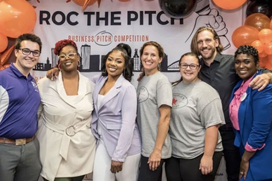 contestants for roc the pitch stand in front of a branded sign and orange balloons