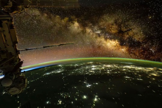 The Milky Way Galaxy glows above Earth with ISS components in the foreground.