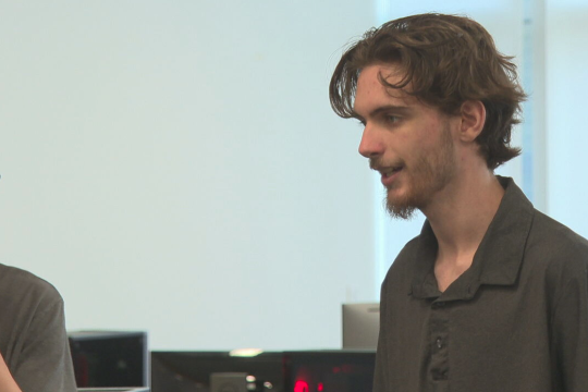Caleb, a local 19-year-old living with a nervous system disorder, watches as people play a video game he created.