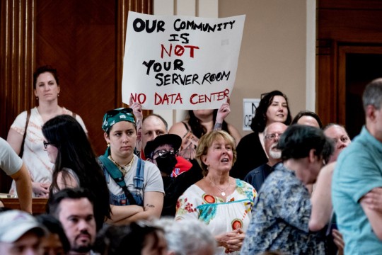 'people crowd in a courtroom holding signs againt flock cameras and data centers'
