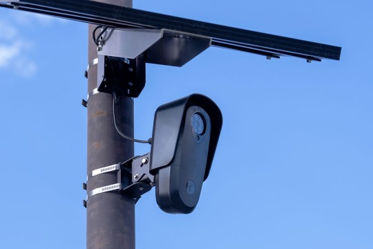 A flock camera stands on top of a pole in the sky