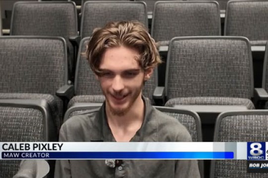 'a young man sits in an auditorium speaking to channel eight news'