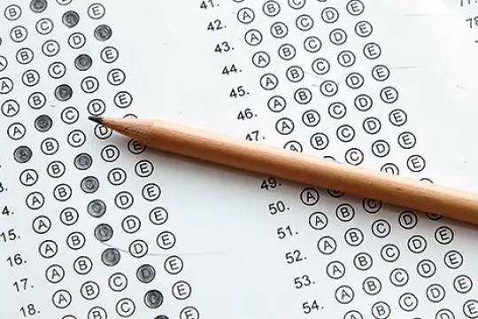 'a round pencil sits on top of a standaardized scantron test sheet with some letters colored in.'