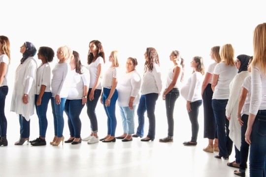 Many women wearing blue jeans and white T-shirts standing in a long line.