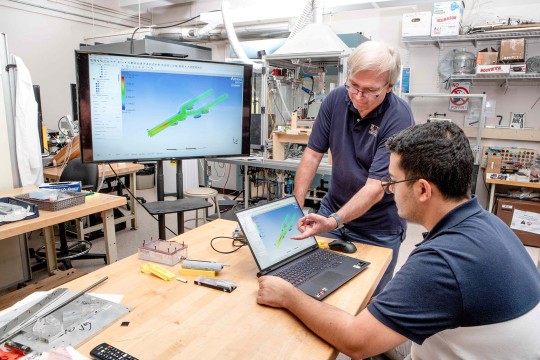 Ed Hensel, standing, associate dean for graduate programs in RIT’s Kate Gleason College of Engineering, works with a student on the design one of the Respiratory Technology Lab’s original wireless Personal Use Monitors. 