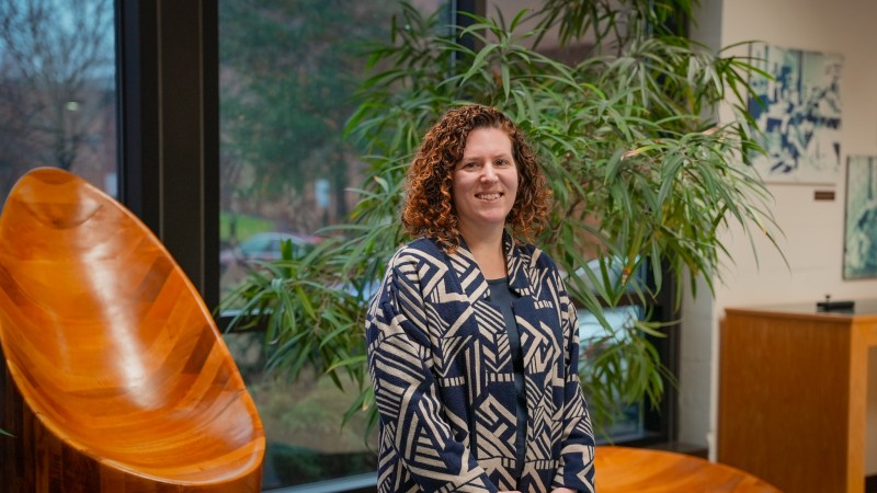 Woman standing in atrium in front of a window with a potted tree.