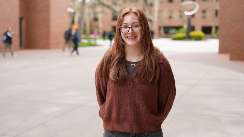 Student standing outdoors in front of brick building, smiling