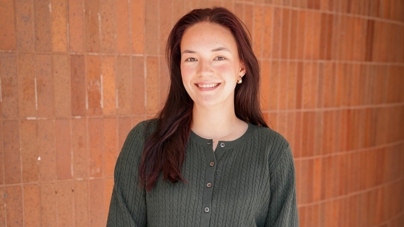 student smiling, posed outdoors in front of brick wall