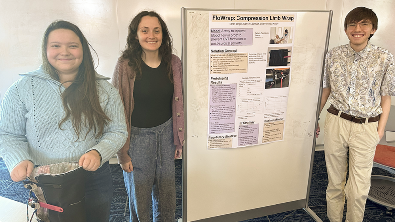 Three RIT Master's students standing on either side of a research poster and smiling.
