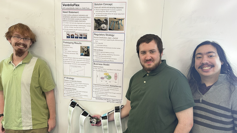 Three RIT Master's students standing on either side of a research poster and smiling.